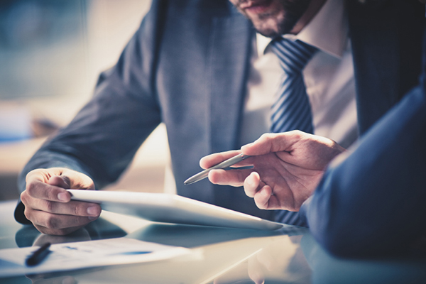 Two men in suits at a conference table discussing a document.